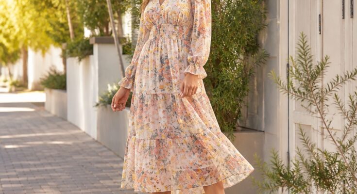 Mulher elegante usando vestido midi floral em tons pastel e botinhas brancas em ambiente externo com árvores ao fundo.