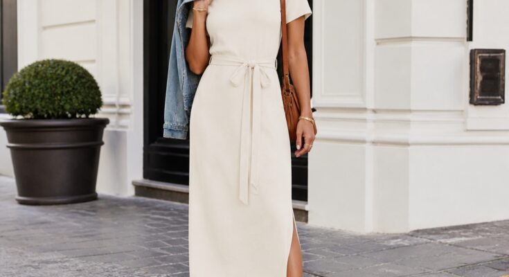 Mulher elegante vestindo vestido midi claro e tênis branco em ambiente urbano iluminado, com pose descontraída.