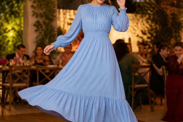 Mulher dançando em festa, usando vestido longo azul serenity, com luzes suaves ao fundo.