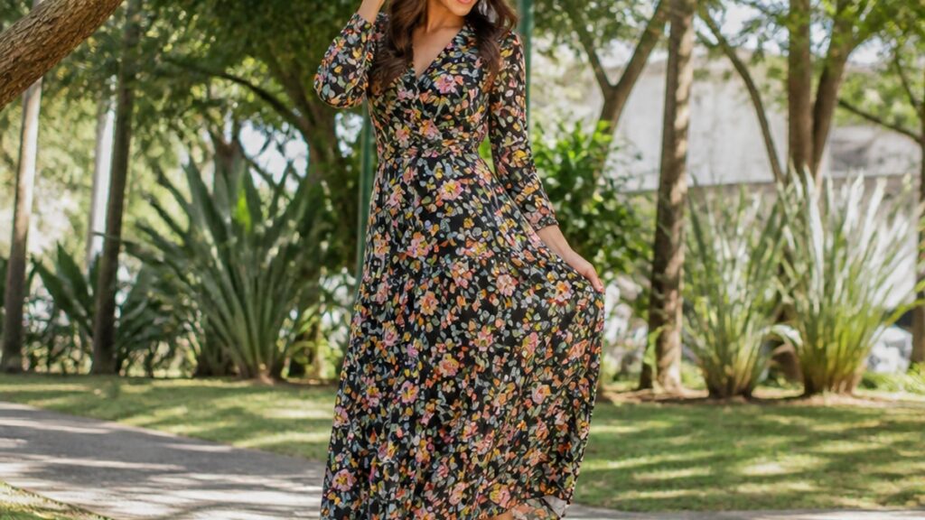 Uma mulher usa um vestido longo florido e botinhas pretas em um parque ensolarado.