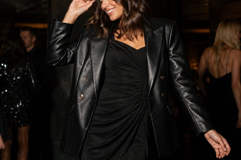 Uma mulher usa blazer de couro sobre um vestido curto em um ambiente festivo.