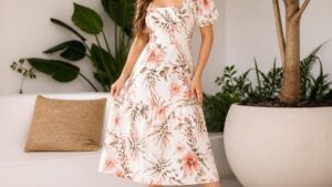 Uma mulher elegante usa um vestido midi florido e sandálias plataforma brancas em um ambiente iluminado com plantas ao fundo.