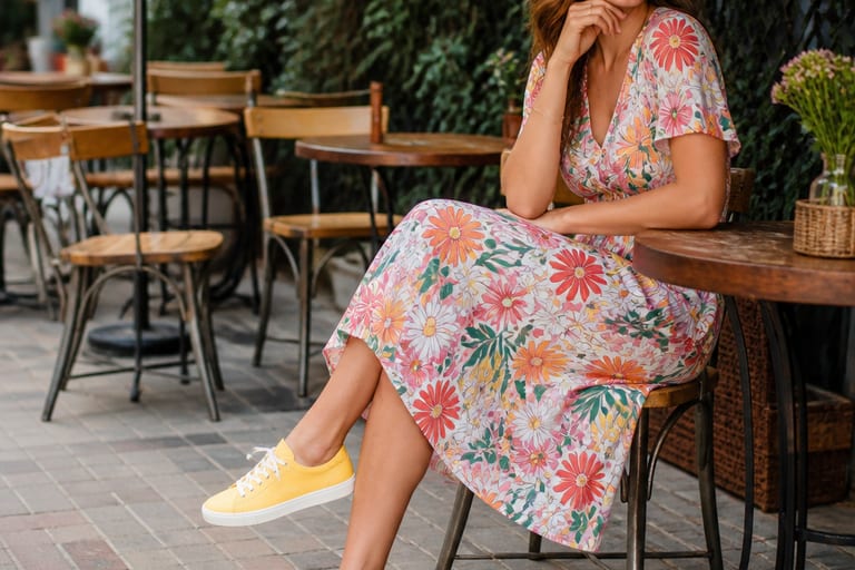 Mulher usando vestido midi floral e sapatenis amarelos em café ao ar livre.